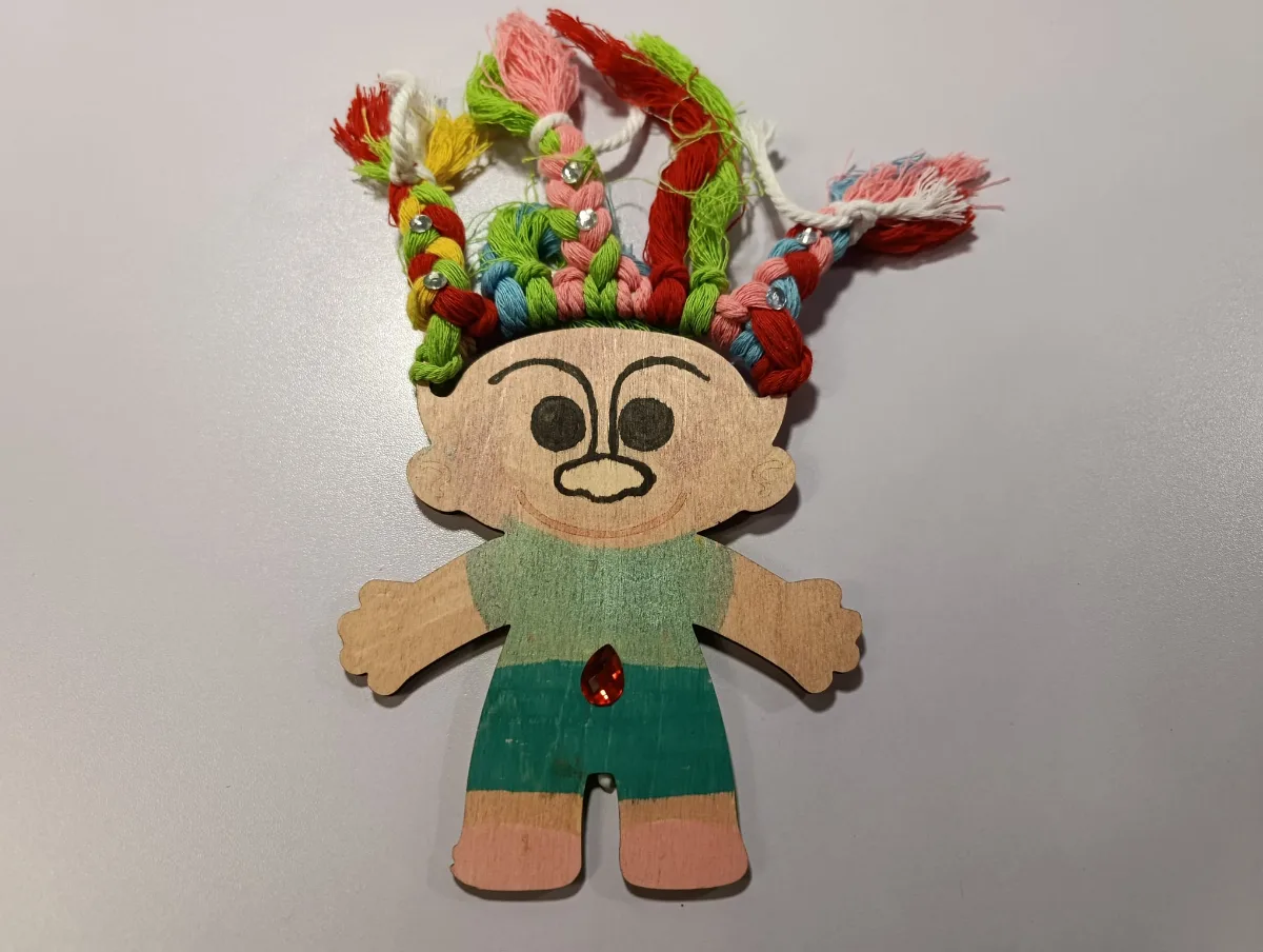 Dřevěná figurka trolla s barevnými ozdobami na hlavě a v rukou.